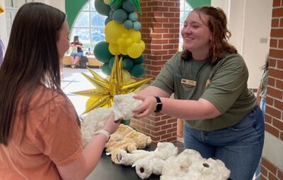 Campus Engagement Chair, Kylie Kelly, handing a student a teddy bear stuffing kit
