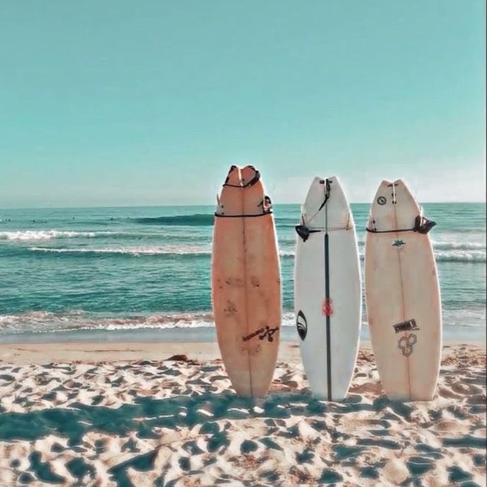 Surfboards on a sandy beach with ocean waves in the background