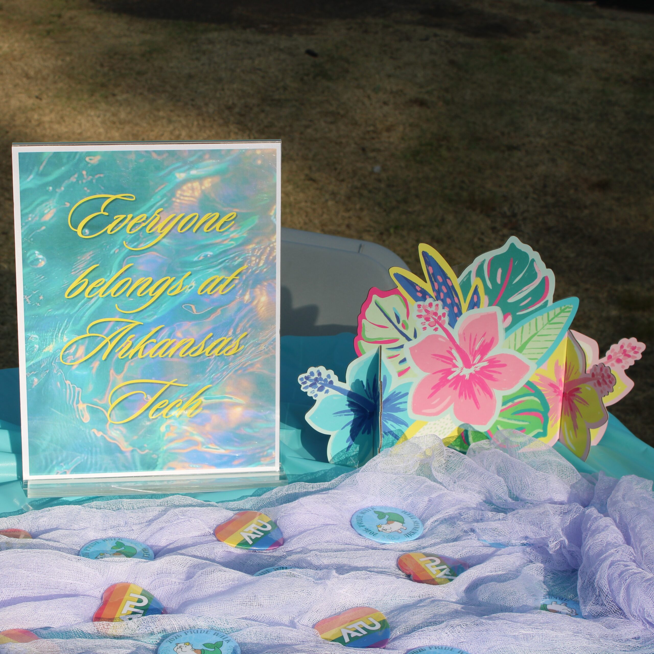 Sign that says "Everyone belongs at Arkansas Tech" on table with pride themed buttons